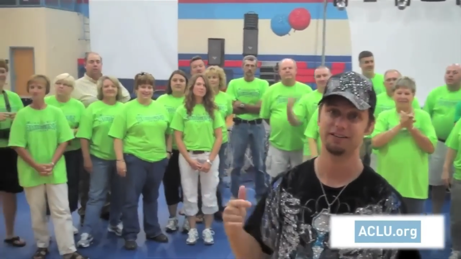 A group of people wearing bright green tshirts stand in a line, with one person in a black tshirt and cap stands close to the camera.