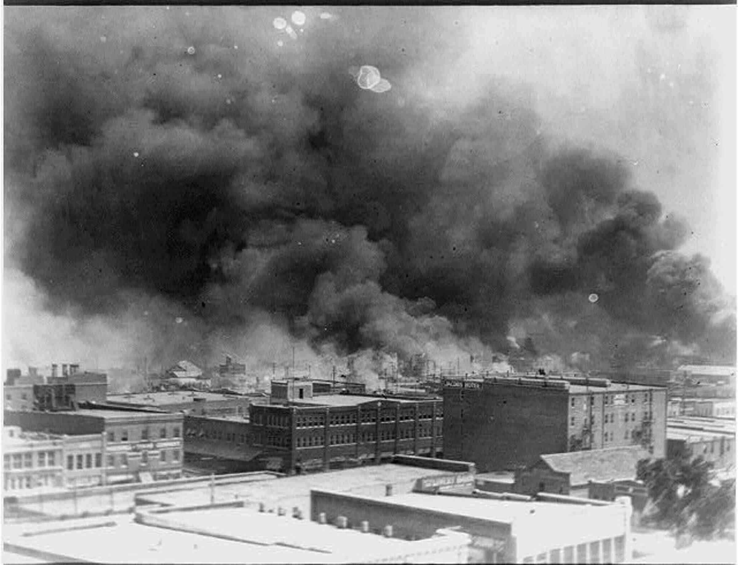 A black and white photo of a building in flames, with a large cloud of smoke in the sky.