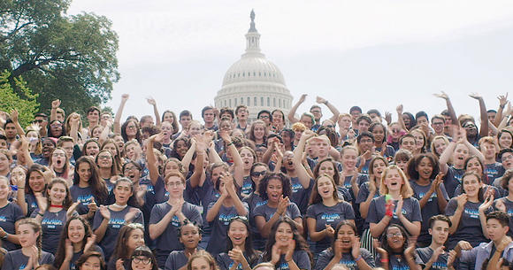 A large group of students waving in front of the US Capitol