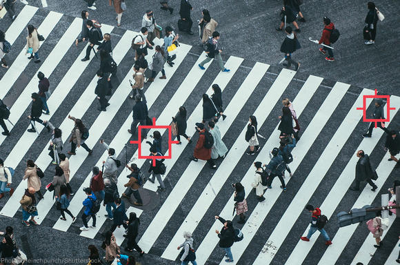 A top level view of many people crossing a street, with red squares around a few people's heads