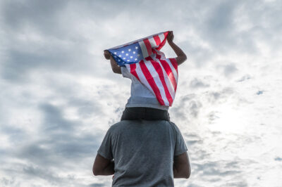 Child holding American flag sitting on dad's shoulders