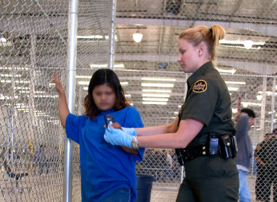 CBP Border Patrol agent conducts a pat down of a female Mexican being placed in a holding facility.