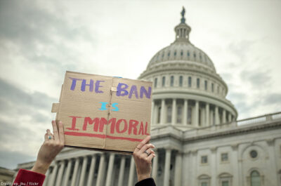 Person holding "The Ban Is Immoral" sign in front of Capitol building