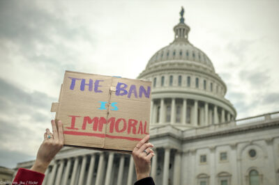 Person holding "The Ban Is Immoral" sign in front of Capitol building