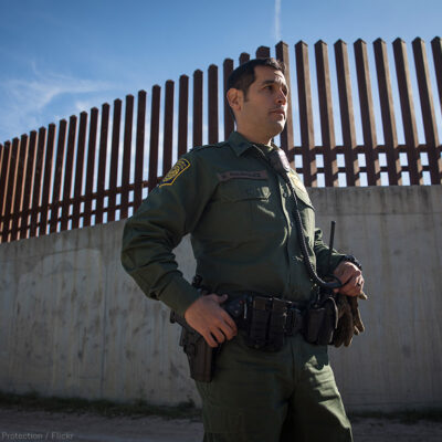 CBP Agent standing before southern border wall.