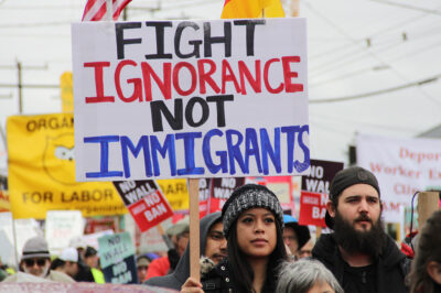 A protester holding a sign with the text "fight ignorance not immigrants"