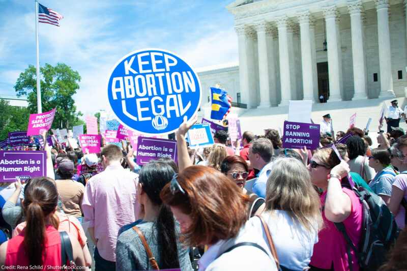 A crowd of pro-choice protesters standing outside the Supreme Court holding up signs that read "Keep Abortion Legal," and "Abortion is a Human Right" among other signs.