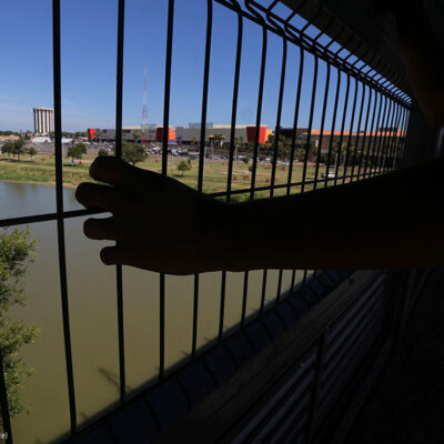 The hand of a youth from Nuevo Laredo rests on the gate as he stops to watch a train pass, above the Rio Grande river on International Bridge 1 Las Americas, a legal port of entry which connects Laredo, Texas in the U.S. with Nuevo Laredo, Mexico, Thursday, July 18, 2019.