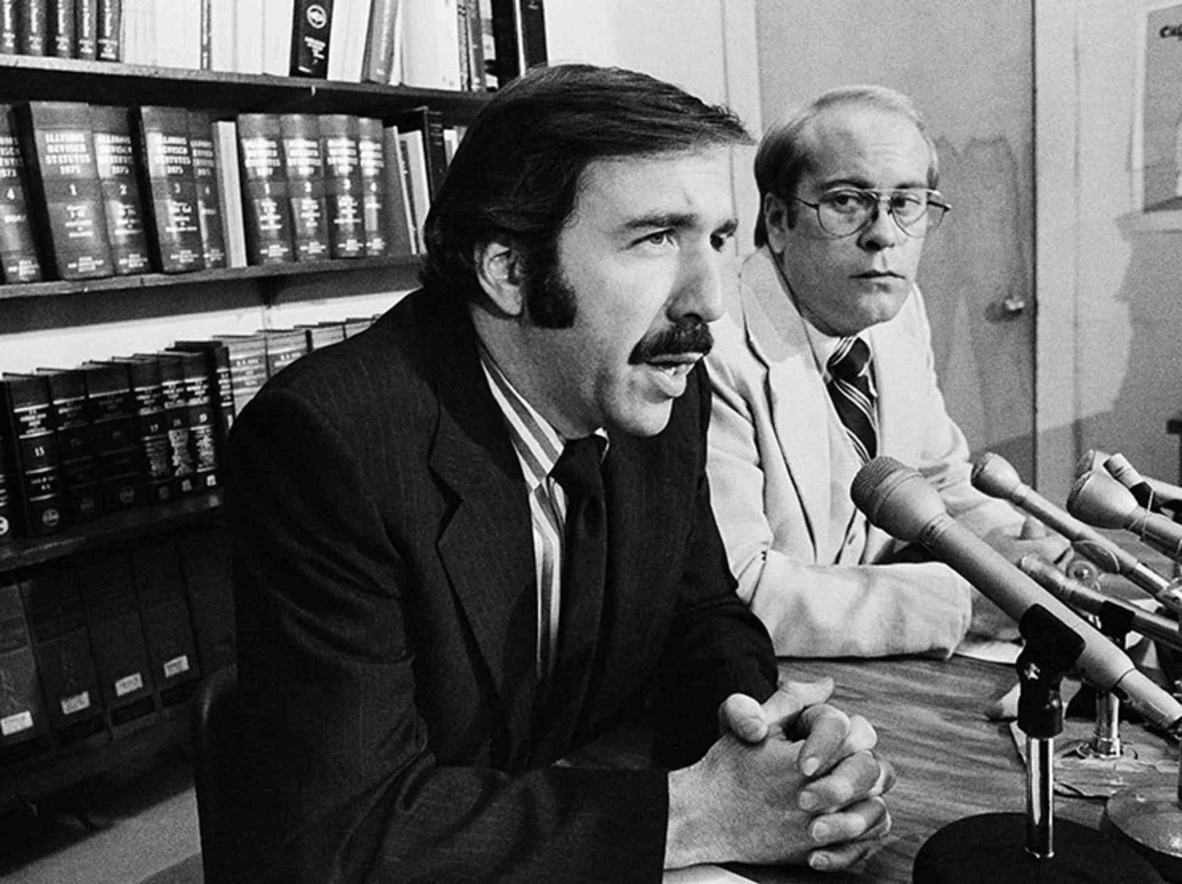 A black and white photo of David Goldberger speaking into many microphones