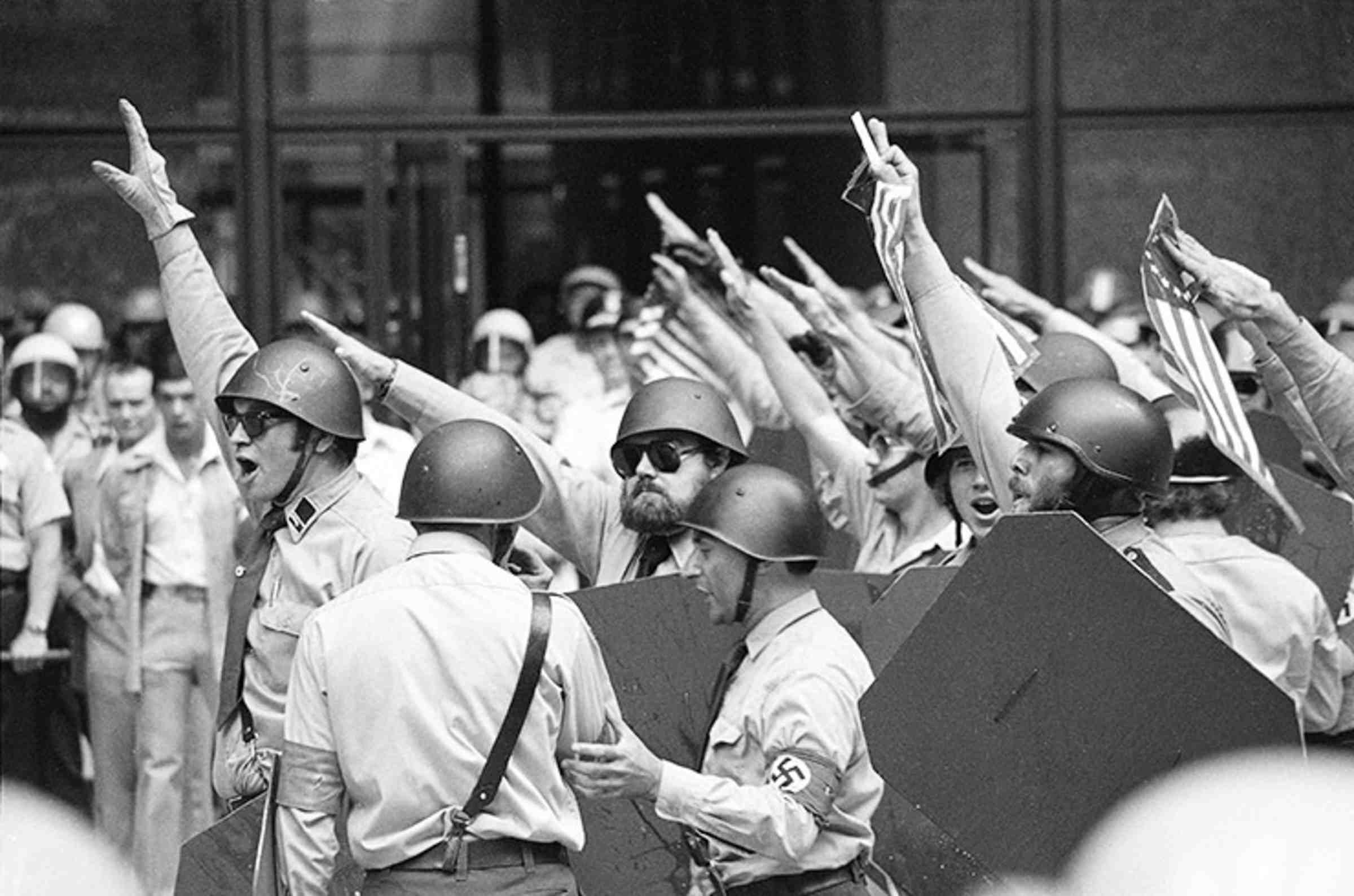 A black and white photo of many men wearing helmets and raising their arm in the air.