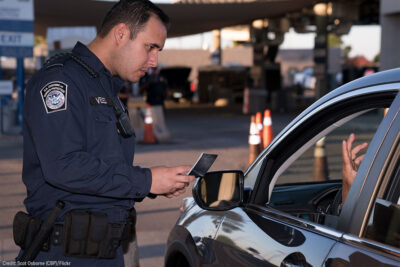 A U.S. Customs and Border Protection checking the identification of someone seated in a car.