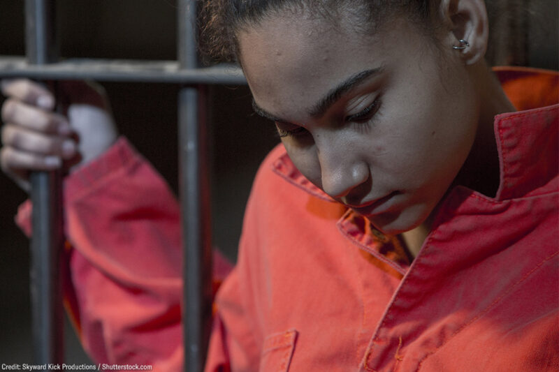 A incarcerated woman standing behind bars.