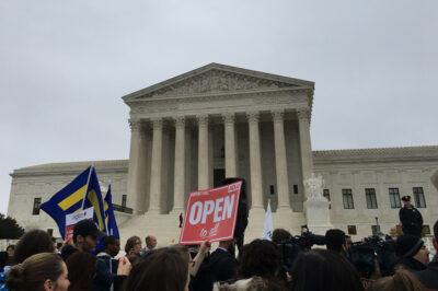Demonstrators outside the Supreme Court with signs advocating for the rights of LGBT people, including a sign with the text "Open to All" in the center.