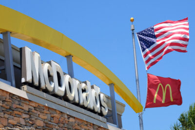 McDonalds logo besides the company flag and the American flag on a flagpole outside of the restaurant chain.