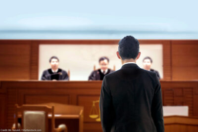 Back of lawyer talking to judges in a courtroom.