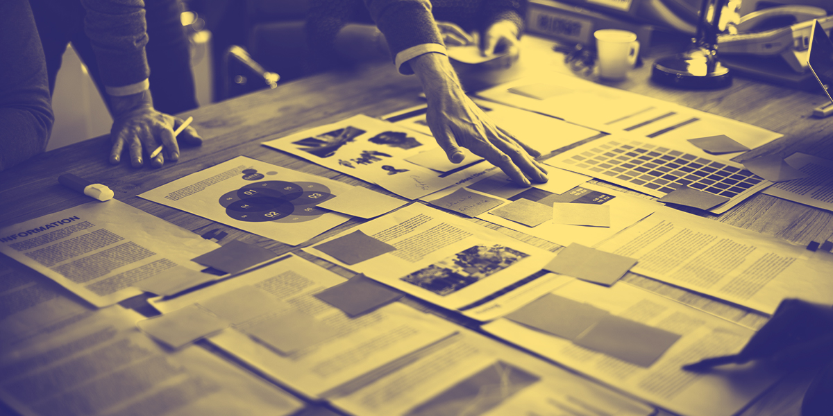 A yellow tinted image of a hand over a number of research papers laid out on a desk