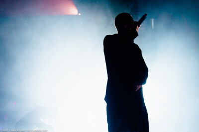 Silhouette of a rapper onstage with bright stage light and smoke in the background.