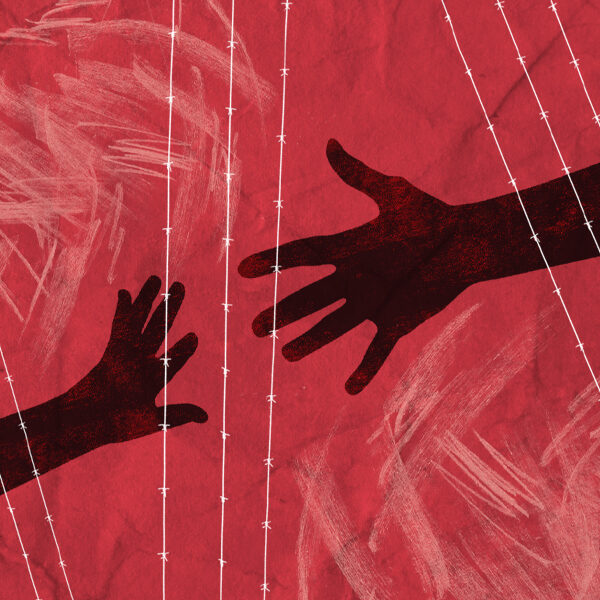 Two hands reaching for one another behind a wired fence