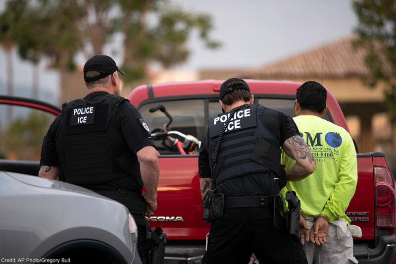 U.S. Immigration and Customs Enforcement (ICE) officers detain someone in front of a red truck.