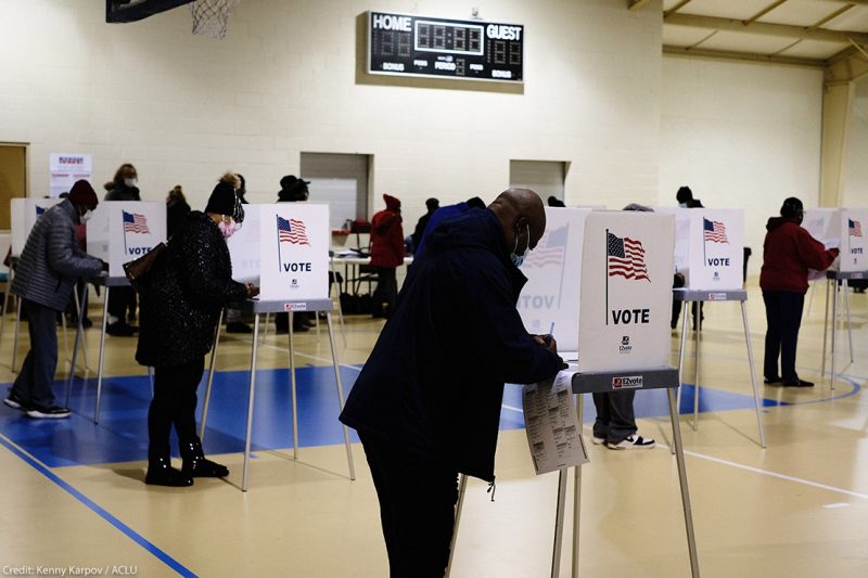 A black man filling out ballot in voting booth on Election Day.