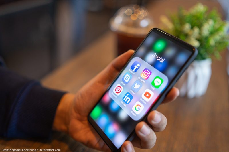 Man holding iPhone with social media icons displayed on the screen