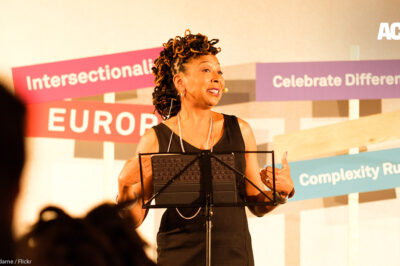 Kimberlé Crenshaw gives presentation at podium with "Intersectionality" and "celebrate differences" sign behind her.