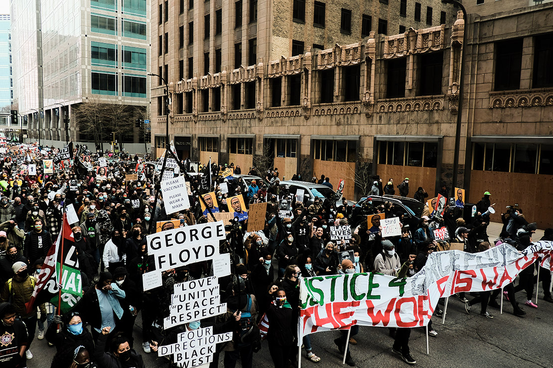 Demonstrators marching and holding signs, protesting the death of George Floyd.