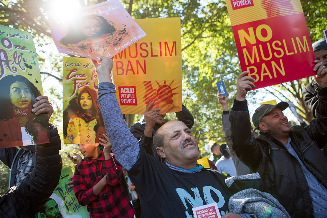 Demonstrators holding signs, one of which says “No Muslim Ban.”