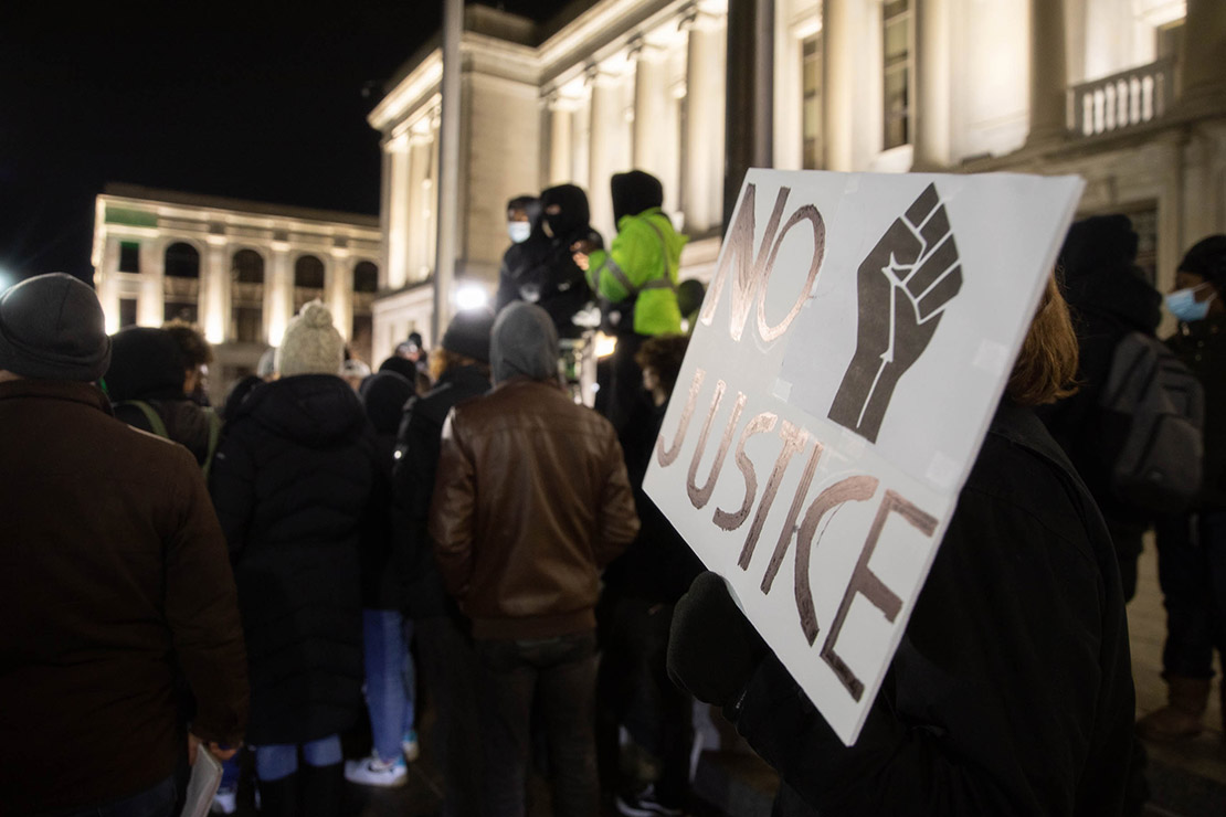 A crowd of demonstrators with one holding a sign reading “No Justice.”