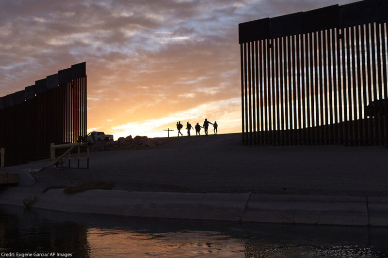 A pair of migrant families at the border wall between the United States and Mexico.