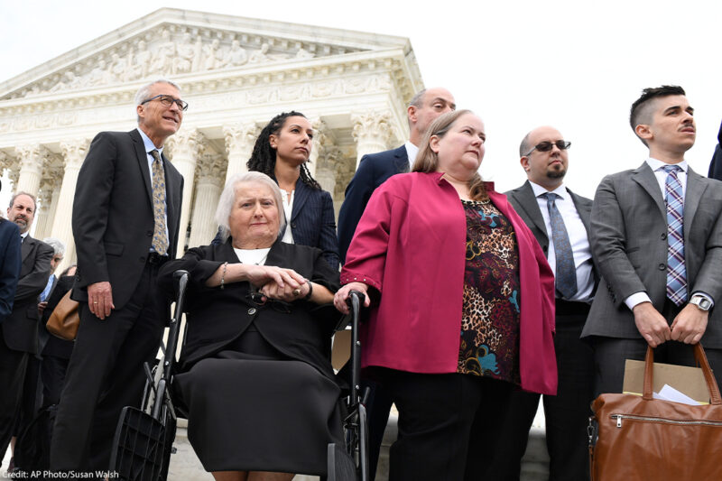 Aimee Stephens, seated, her wife Donna Stephens, in pink, and ϰſ attorney Chase Strangio, at the far right listen during a news conference outside the Supreme Court.