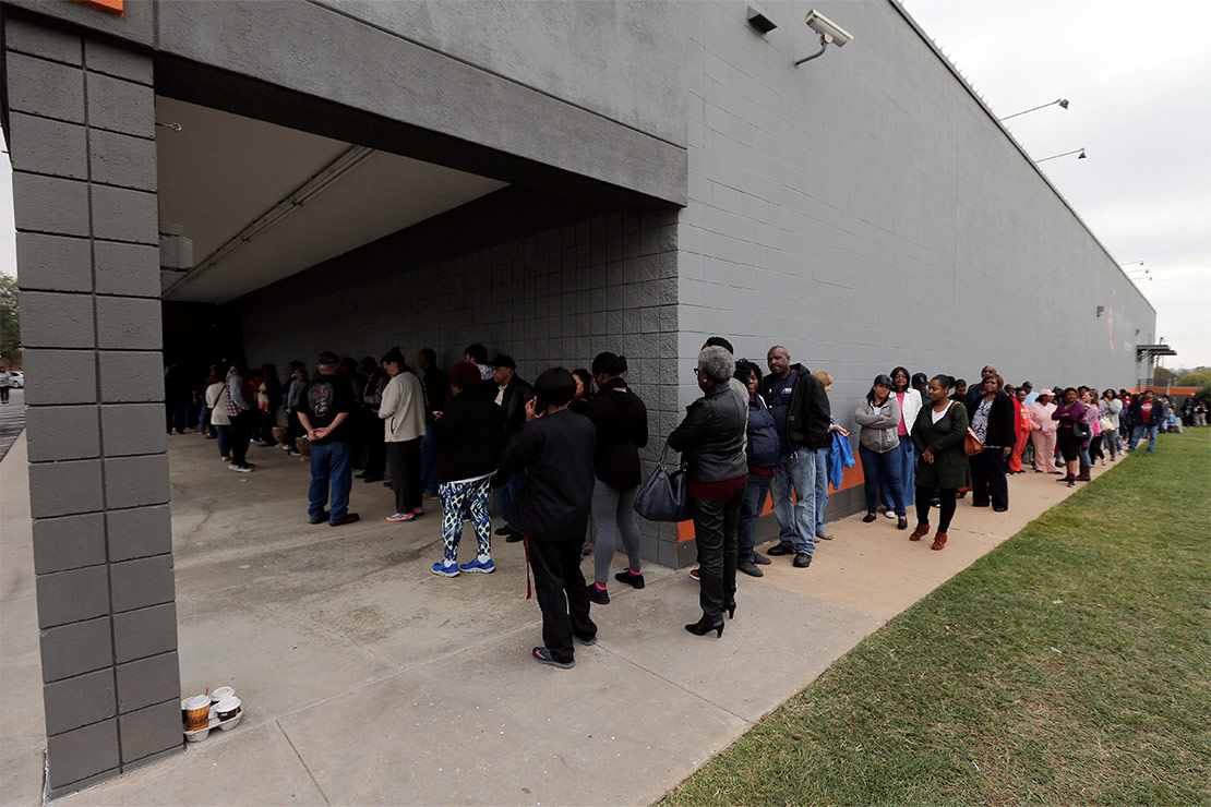 Voters, mostly black, line-up to vote on a queue that snakes along the perimeter outside the building of a polling station.