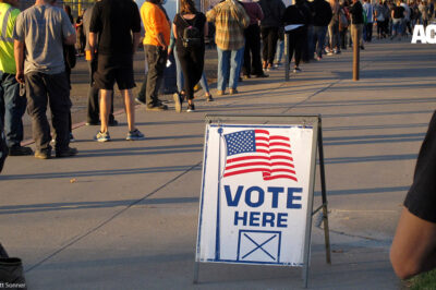 A sign that says "vote here" among a line of voters.