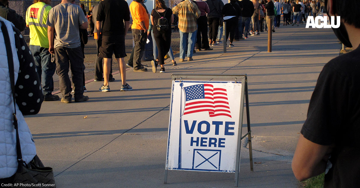 A sign that says "vote here" among a line of voters.