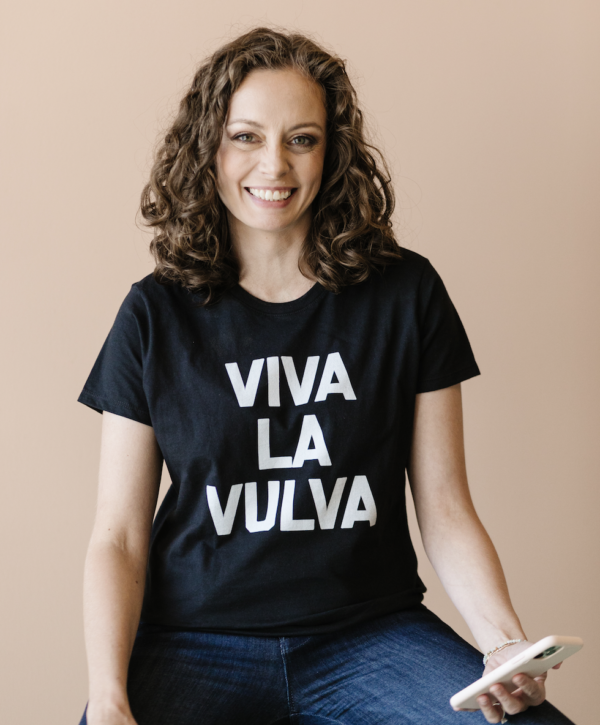 Dr. Jennifer Lincoln is a white woman with brown hair. She is against a beige backdrop wearing a black tshirt that says "viva la vulva" in white letters.