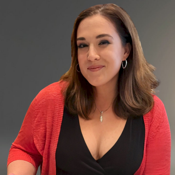 Headshot of Margaret Huth smiling closed-mouth. She is wearing a black v-neck blouse with a coral cardigan over it.