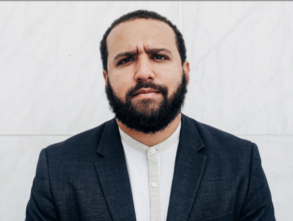 Headshot of Wesley Lowery with a neutral expression. He is wearing a dark gray blazer over a white buttoned shirt