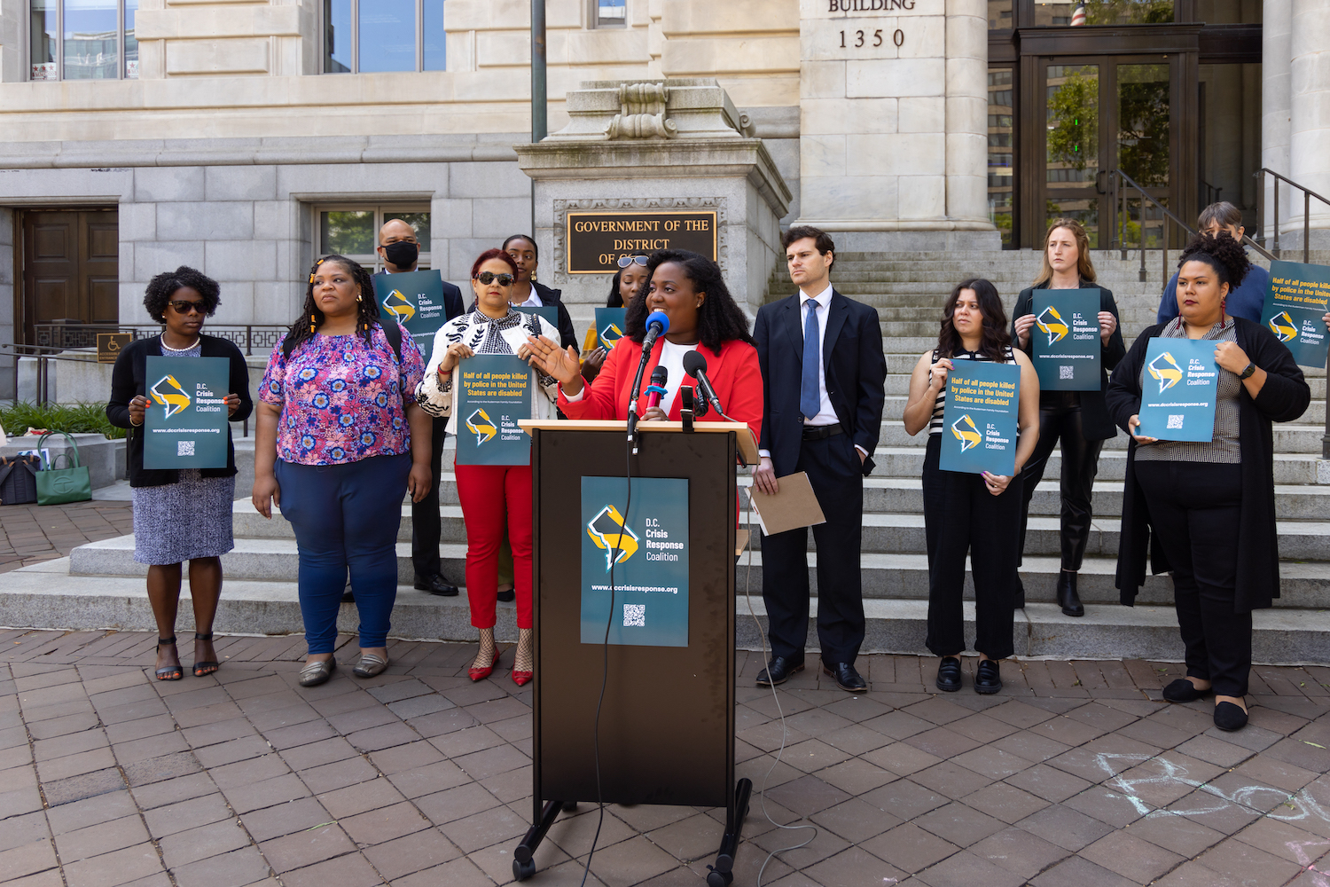 Members of the DC Crisis Response Coalition speaking at an outdoor event.