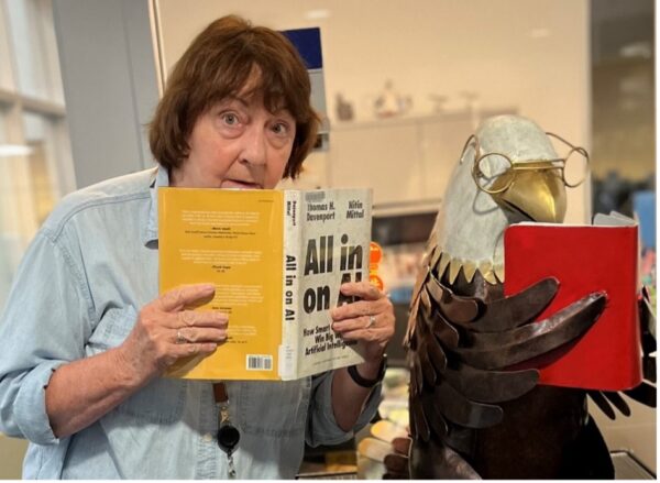 Headshot of librarian Deborah Hall. She's holding a book to her face and standing next to a statue of an eagle holding a book.