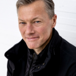 Headshot of sociologist Matthew Desmond smiling, closed-mouth. He is wearing a black jacket.