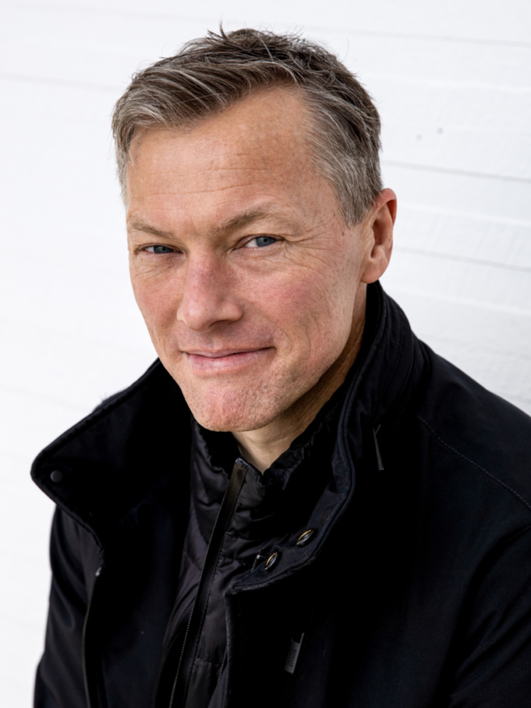 Headshot of sociologist Matthew Desmond smiling, closed-mouth. He is wearing a black jacket.