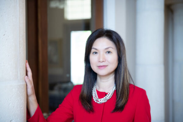 Headshot of attorney Echo King with a closed-mouth smile, She is standing in front of a building with a glass door, and wearing a red cardigan and pearl necklace.