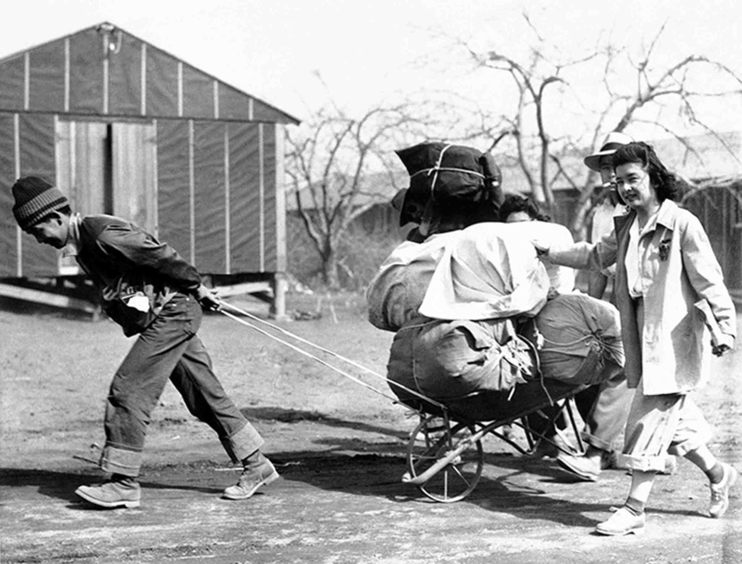 A black and white photo of someone pulling a wagon full of bundled parcels