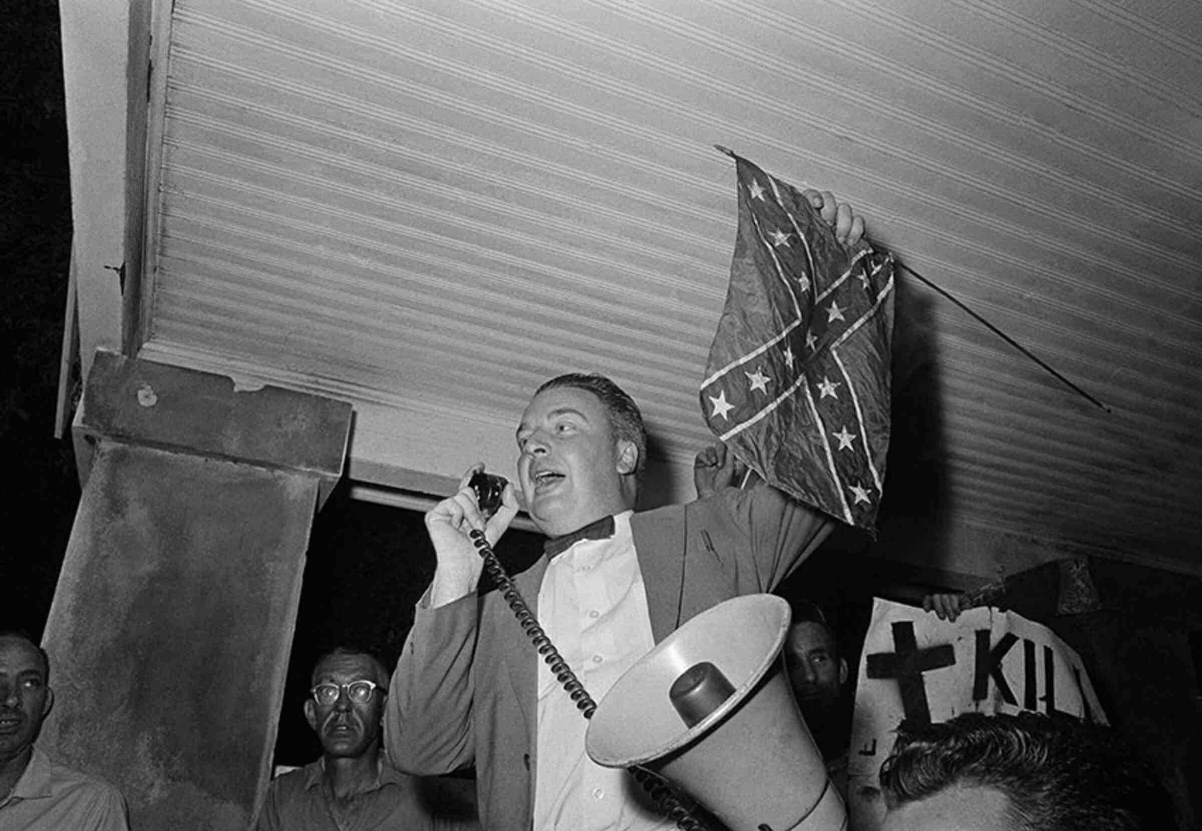 J.B. Stoner holding a confederate flag and speaking into a megaphone