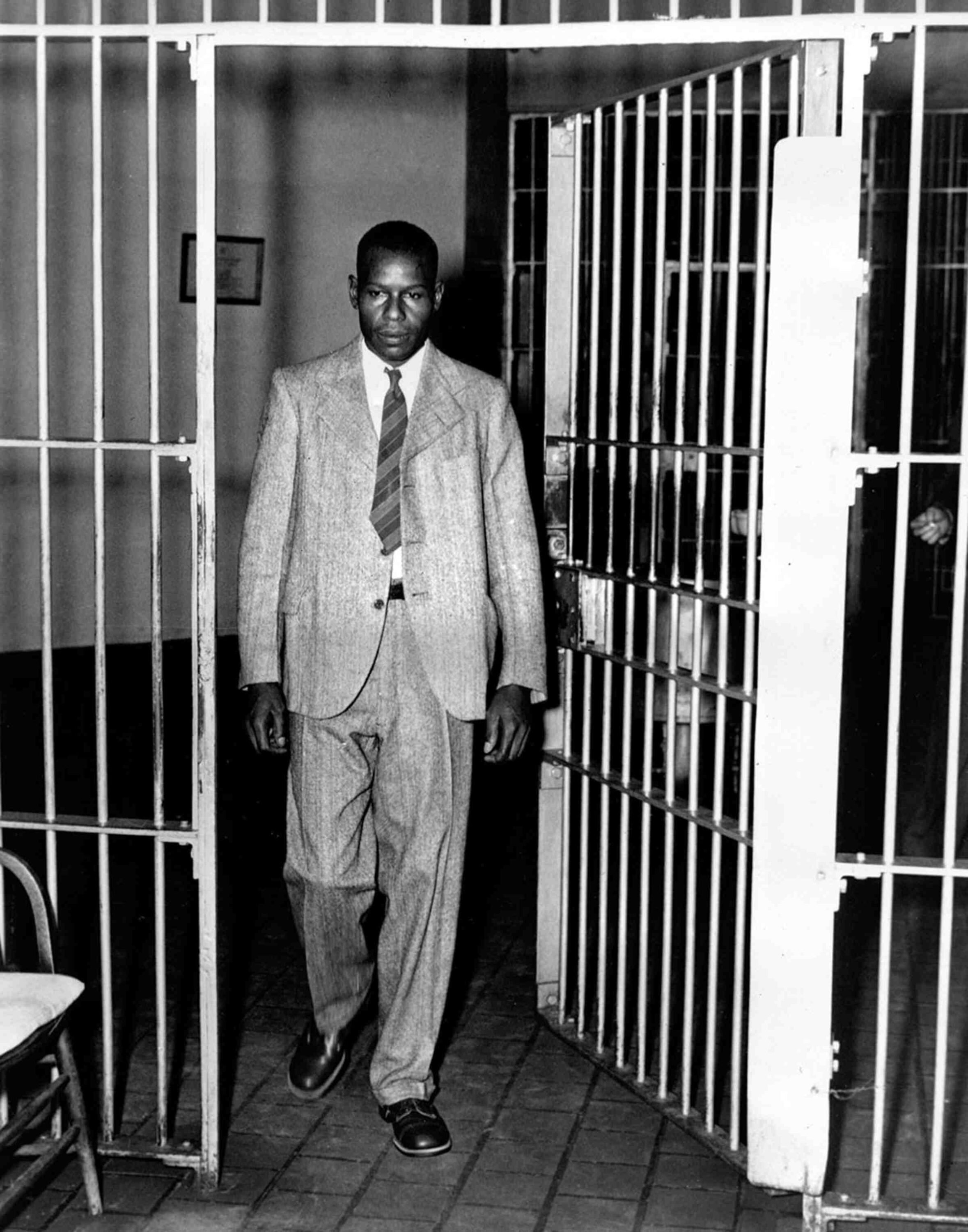 A black and white photo of Clarence Norris wearing a suit and tie, walking out of a jail cell.