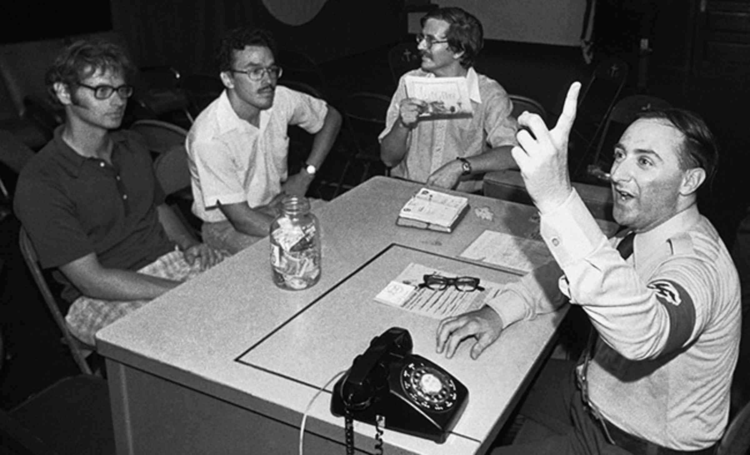 A black and white image of four men sitting around a table, one wearing a swastika armband