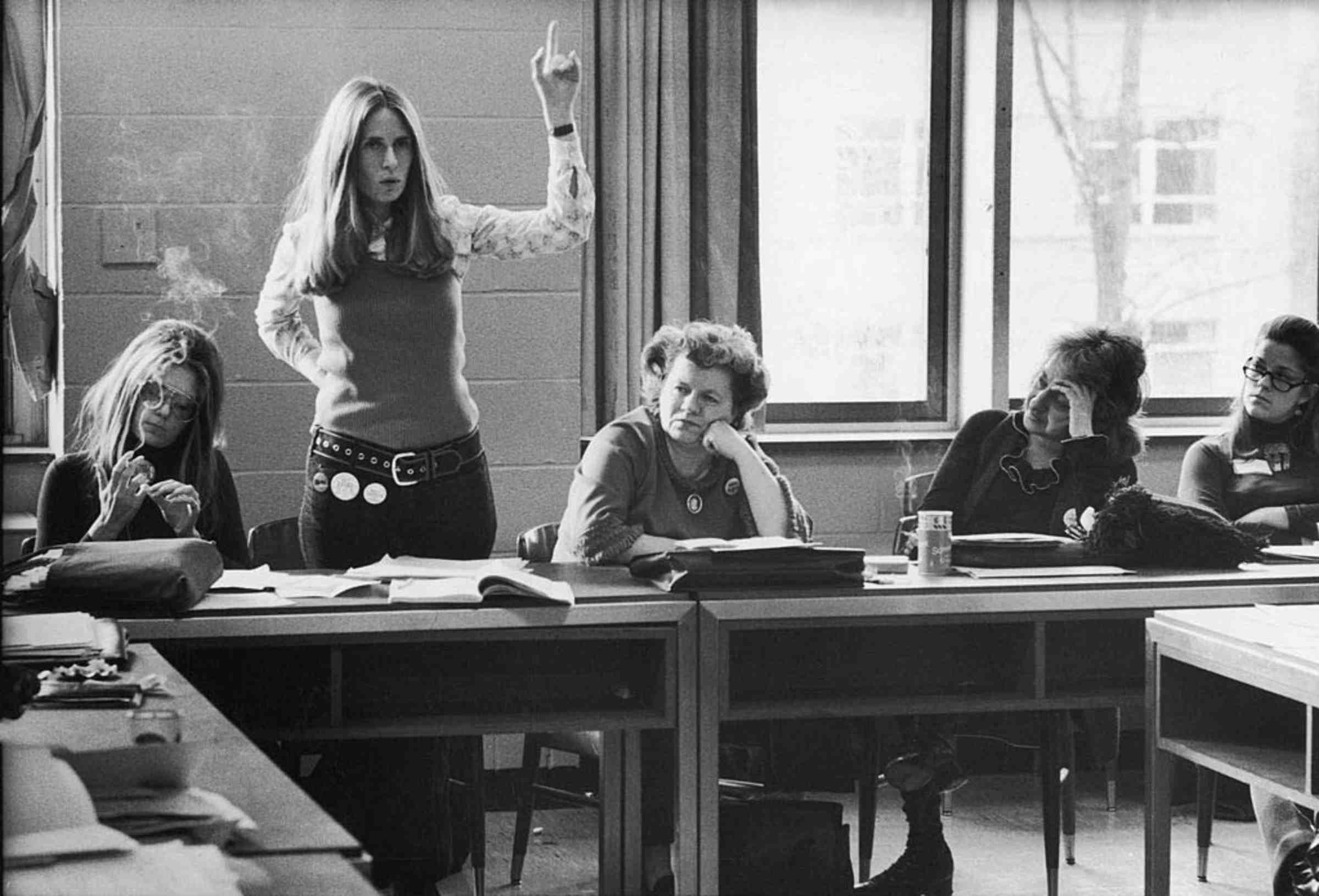 Fve people in a classroom, with one woman standing with her arm raised