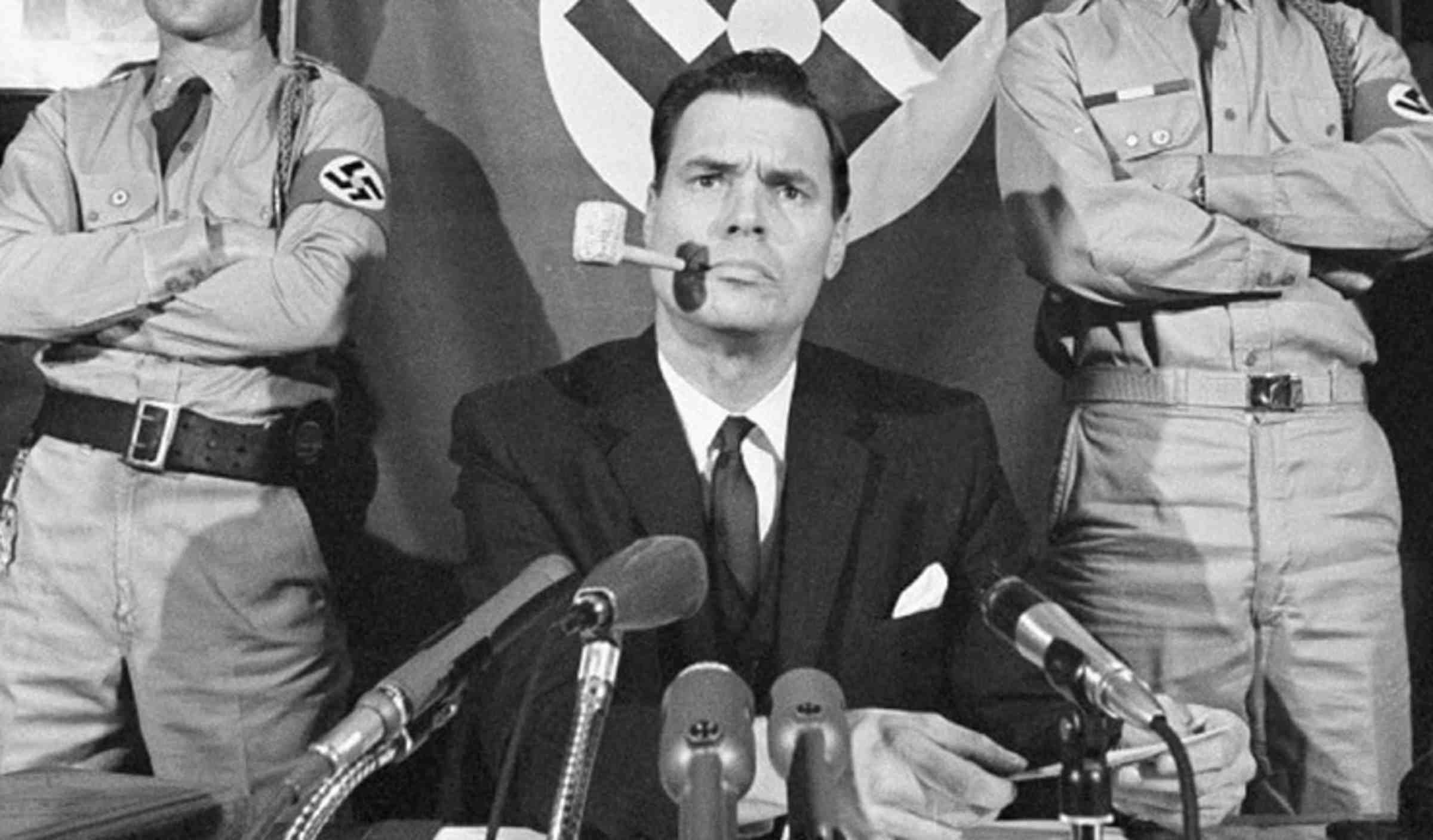 A black and white photo of a George Lincoln Rockwell flanked by two people wearing swastika armbands