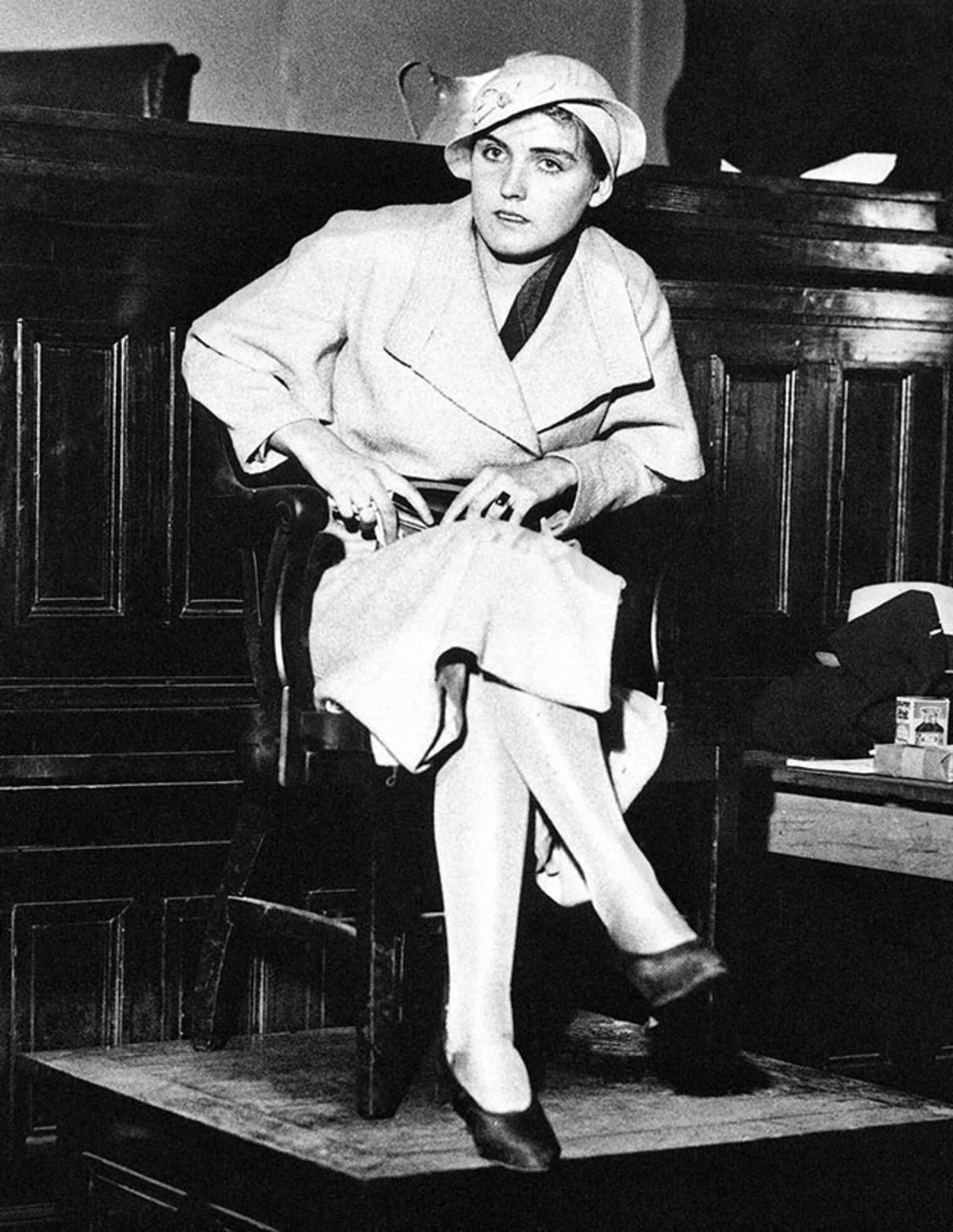 A black and white photo of Ruby Bates sitting in a courtroom wearing a hat and long coat.