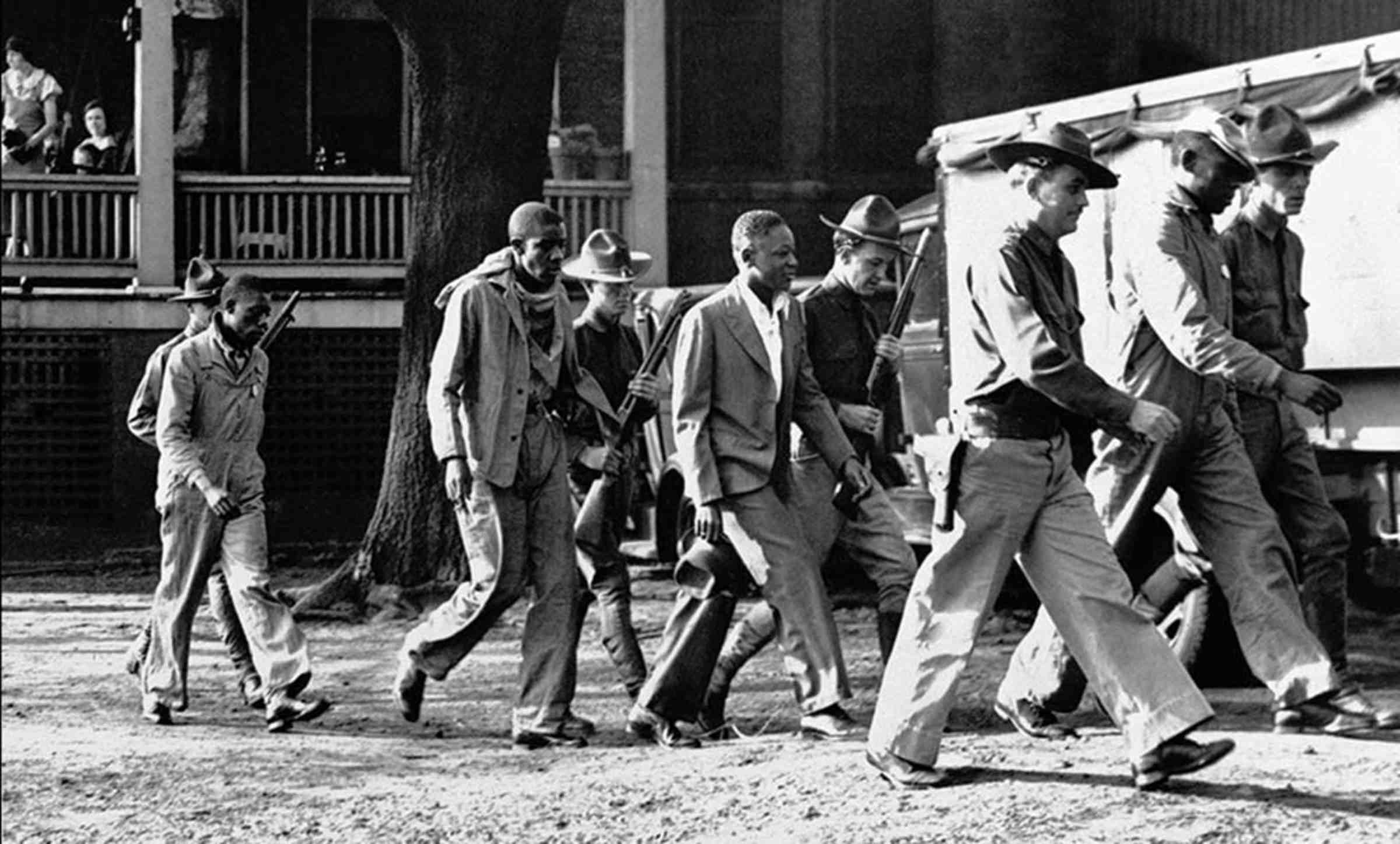 A black and white photo of the Scottsboro boys and armed guards.